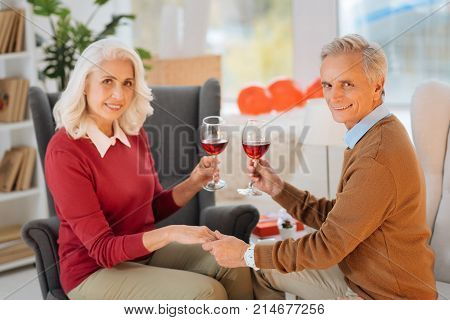 Love never dies. Selective focus on a smiling elderly gentleman looking into the camera while holding a hand of his beautiful wife during their marriage anniversary celebration.
