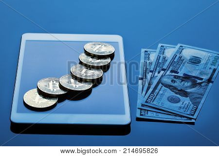Coins of crypto-currency bitcoin and hundred-dollar bills with a tablet computer.  Tinting in blue. The concept of virtual business and currency.