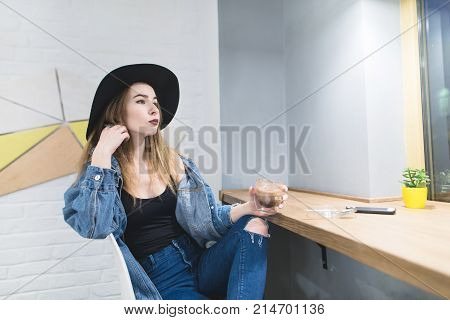 Stylish hipster woman posing in a cozy cafe. Portrait of a stylish girl in a modern cafe for a cup of coffee