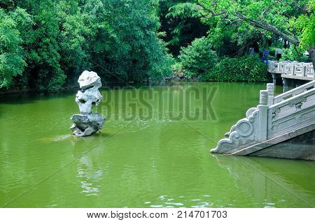 An outdoor rock sculpture over the green water as stone steps lead down to the water's edge on Fairy Island on Lake Tai (taihu) in Wuxi China in Jiangsu province.