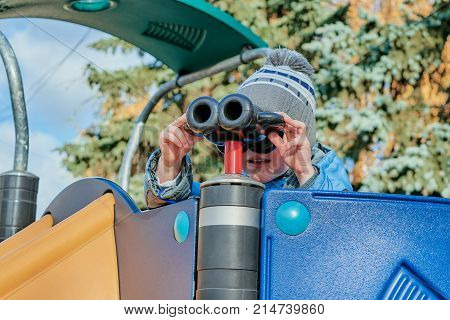 Little boy looking through binoculars on a slide at the Playground. The boy is holding the binoculars with your hands and looking for something in the distance.