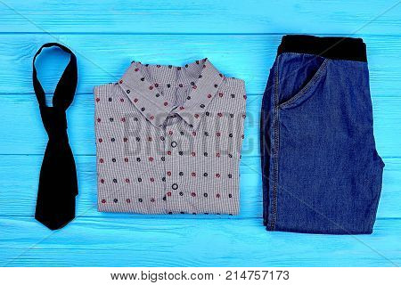 Set of trendy clothes for toddler boys. Tie, shirt, jeans for little boy on blue wooden background. Little boy fashion clothes on sale.