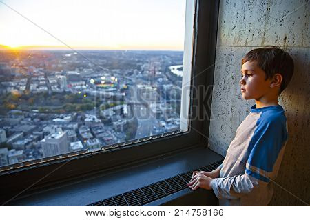 thoughtful boy standing at the window. the child looks at the city from the window of the skyscraper. Copy space for your text