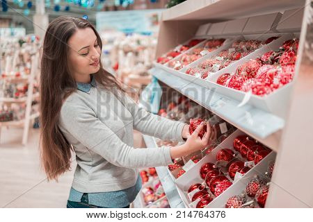 Cheerful happy customer girl choosing gifts for Christmas and New Year. She is taking Christmas tree decorations