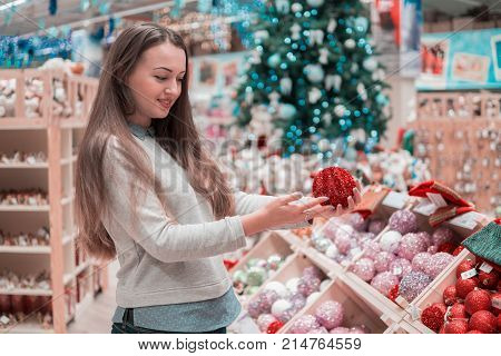 Cheerful happy customer girl choosing gifts for Christmas and New Year. She is taking Christmas tree decorations. difficult decision. Various choice