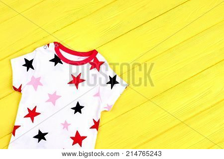 Baby stars print soft t-shirt. Baby boy or girl short sleeve bodysuit on yellow wooden background.