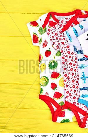 Babies new brand rompers, top view. Set of beautiful infants rompers on yellow wooden background, top view.