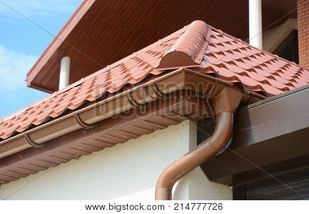 Close up on roof gutter holder and guttering downspout pipe with clay tiles roof. Installing rain gutter.