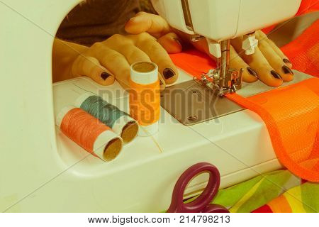 woman's hands using sewing machine with reels of colour threads. Workplace of tailor. people needlework and tailoring concept - tailor woman threading needle of sewing machine