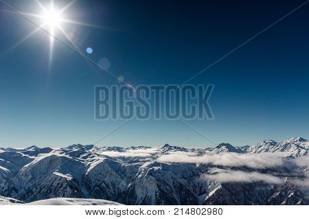 Scenic view of high winter mountains covered with snow under the clouds in the clear blue sky
