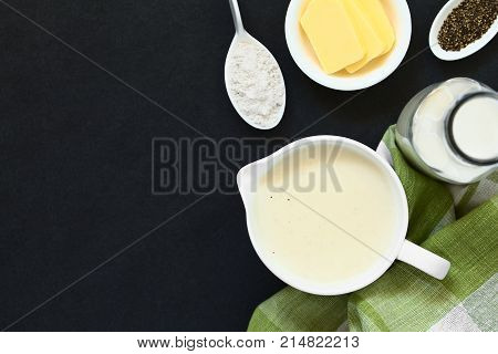 Homemade French Bechamel or White Sauce served in sauce boat with ingredients on the side (flour butter milk pepper) photographed overhead on slate with natural light (Selective Focus Focus on the sauce)