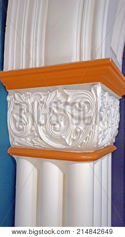 Column supporting an arch indoors. Pillar made of white plaster and decorated with white bas-relief architectural detail.