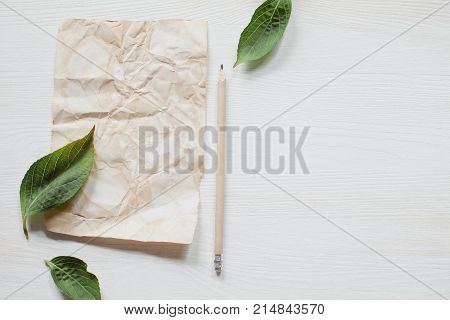 Rustic sheet of paper with pencil and leaves on white wooden table