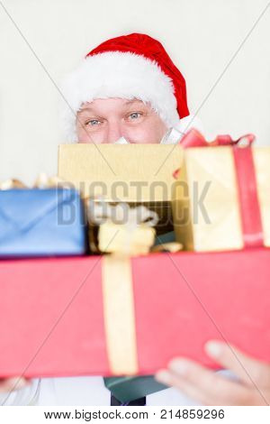 Santa Claus holding stack of Christmas presents and ready for gift-giving. Mature man hiding behind heap of gifts. Happy job concept