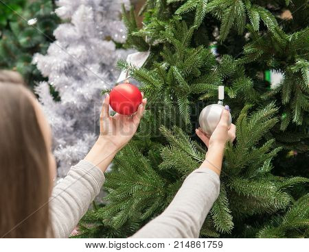 Cheerful happy customer girl choosing Christmas tree decoration balls. difficult decision. Various choice