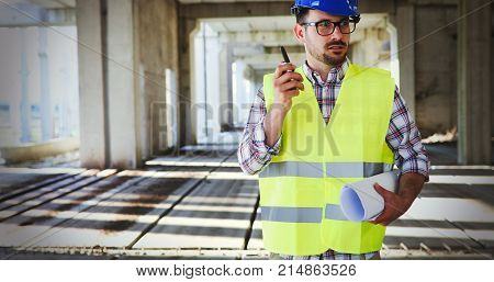 Male architect with blueprints using walkie-talkie at construction site