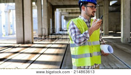 Male architect communicating on walkie-talkie at building site