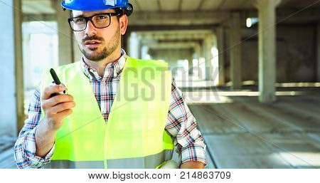 Male architect communicating on walkie-talkie at building site
