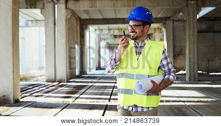 Male architect with blueprints using walkie-talkie at construction site