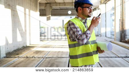 Male architect with blueprints using walkie-talkie at construction site