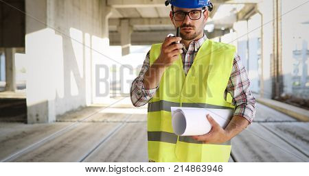 Male architect communicating on walkie-talkie at building site