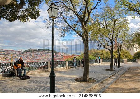 LISBON, PORTUGAL - NOVEMBER 4, 2017: Sao Pedro de Alcantara viewpoint (Miradorou) in Bairro Alto neighborhood with a musician singer in the foreground and the city in the background