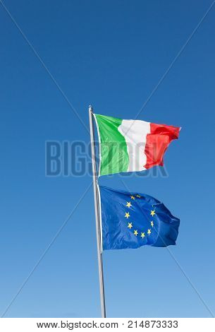 Flags of Italy and Europe waving in the wind on blue sky background.