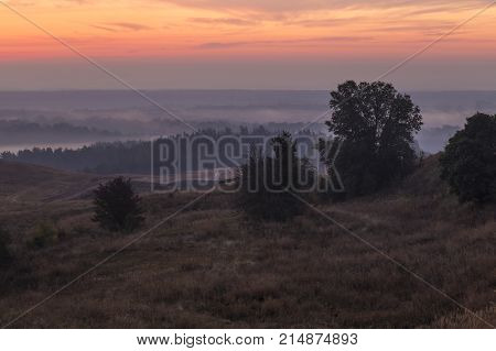 Morning autumn landscape: fog over hills and forest on background of red sunrise. View from above. Village Opishnya Poltava region Ukraine