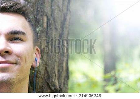 A young man sits under a tree and listens to music