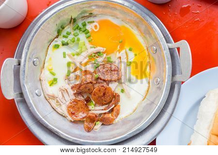 A pan fried egg with toppings on the red tablethis is breakfast of asian food view from top.