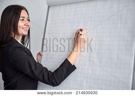 Attractive smiling young woman writing on a blank flipchart in an office as she does a presentation or promotion