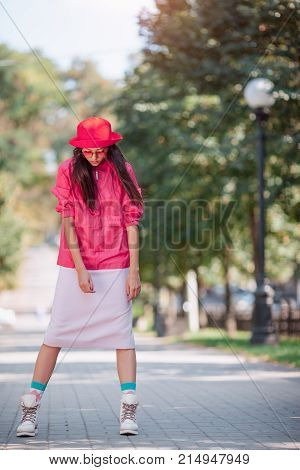 Asian woman fashion photo. Beautiful mixed race asian caucasian young girl in pink hat jaket boots and red sunglasses outdoor against green blurred bokeh nature background. Gorgeous slim model posingi n trendy casual colourful in full-length clothes outsi