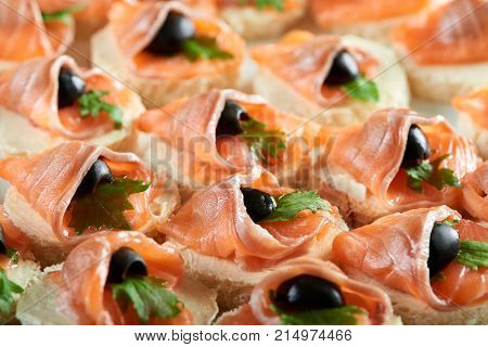Cropped clos up of buttered canapes with smoked salmon decorated with black olives eating food tasty meny serving delicacy gourmet cafe restaurant appetite hunger concept.