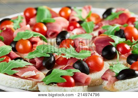 Close up of a plate of delicious tasty ham canapes with cherry tomatoes and black olives decorated with fresh rucola leaves greens healthy delicious organic food eating gourmet concept.