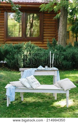 romance, marriage, countryside concept. in the center of great green garden and wooden gouse on the background there is lovely place for couple of newlyweds with soft cushions and candles