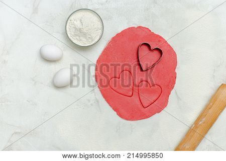 Red Dough With A Cut Out Hearts, Eggs, Flour And Rolling Pin,on A White Table. Top View