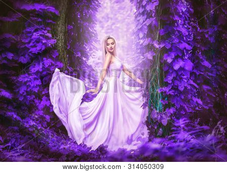 Beauty romantic young woman in long chiffon dress with gown posing in the fantasy forest in violet lush. Beautiful happy bride model girl enjoying nature outdoors, fluttering dress. Autumn garden