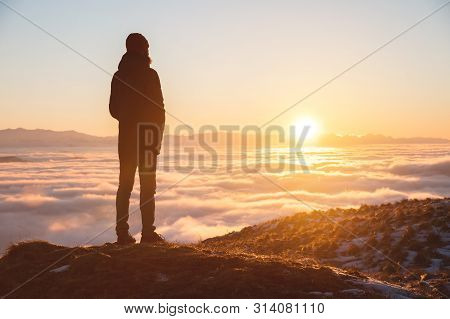 View From The Back. A Lonely Standing Man High In The Mountains Looks At The Setting Sun And The Sun