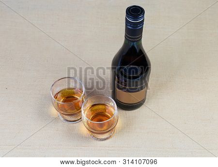 Two Portion Of Brandy In Brandy Bowls And Bottle Of Brandy On A Textile Surface