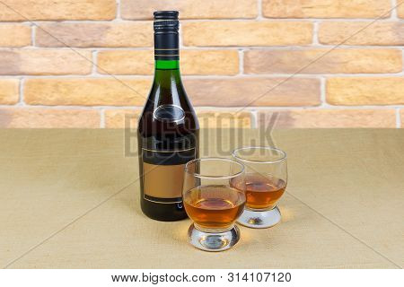Two Portion Of Brandy In Brandy Bowls And Bottle Of Brandy On A Textile Surface