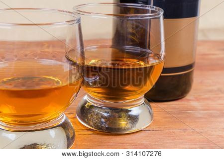 Two Portions Of Brandy In Brandy Bowls On A Blurred Background Of Bottle Of Brandy On The Rustic Tab