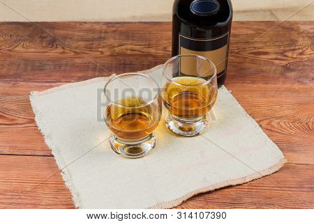 Two Portions Of Brandy In Brandy Bowls On Napkin On A Background Of Brandy Bottle On The Rustic Tabl