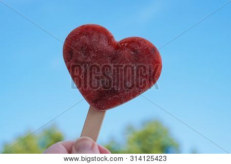 Hand Holding Heart Shaped Homemade Berry Popsicle Or Ice Lolly Against Clear Blue Sky - Love Summer 