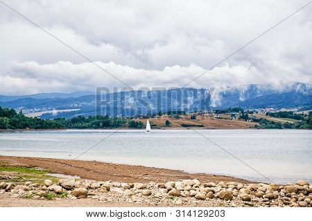 Sailing Boat With A White Sail On The Calm Lake Czorsztyn. Beautiful Mountains, Dramatic Sky. Niedzi