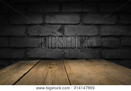 Old Wood Table With Blurred Concrete Block Wall In Dark Room Background.