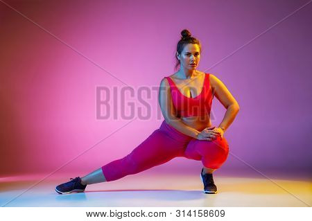 Young Caucasian Plus Size Female Models Doing Exercises On Gradient Purple Background In Neon Light.