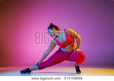 Young Caucasian Plus Size Female Models Doing Exercises On Gradient Purple Background In Neon Light.
