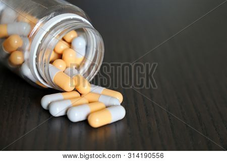 Capsules Spilled From The Bottle, White-yellow Pills On Vintage Dark Wooden Table. Concept Of Pharma