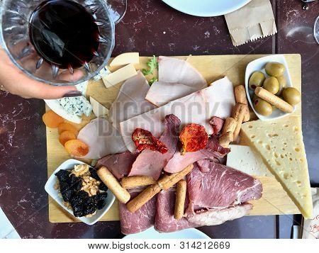 Red Wine And Assorted Cheese Plate, Smoked Beef, Ham, Salami, Green Olives With Fruit For Party.