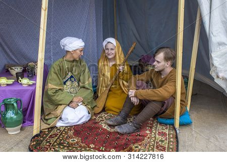 Moscow/ Russia - 15.06.2019: Two Girls And A Guy In Bright Ancient Historical Dresses Sit On A Red T